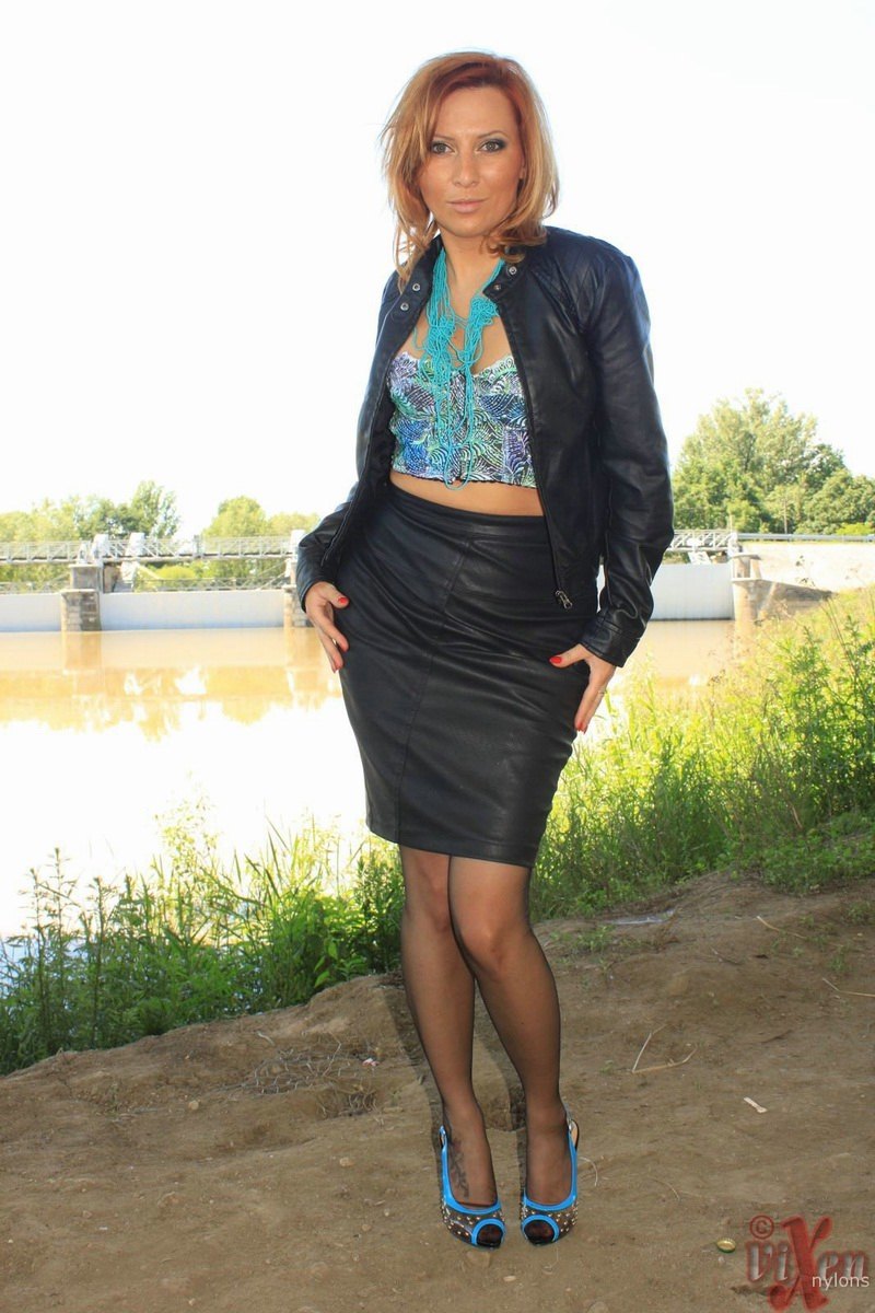 Clothed woman removes leather jacket and skirt by river in nylons and garters